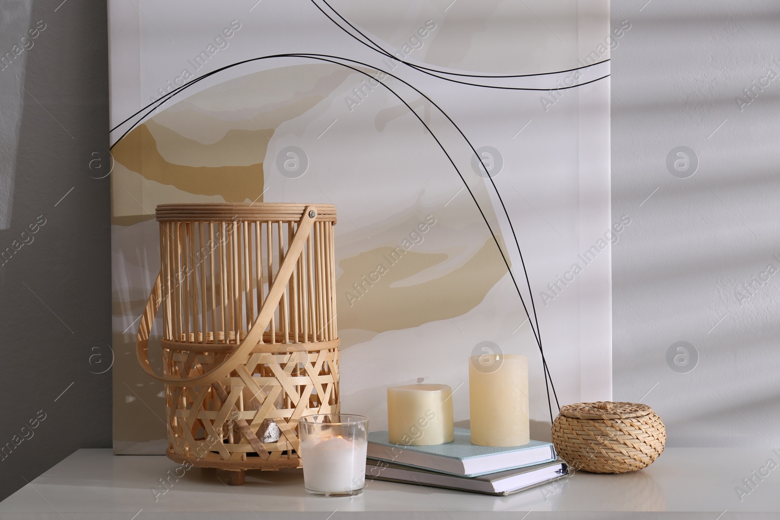 Photo of Burning scented candles and books on white table near light wall