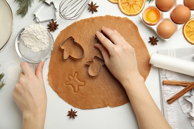 Photo of Woman cutting dough with cookie cutter at white table, top view. Christmas biscuits