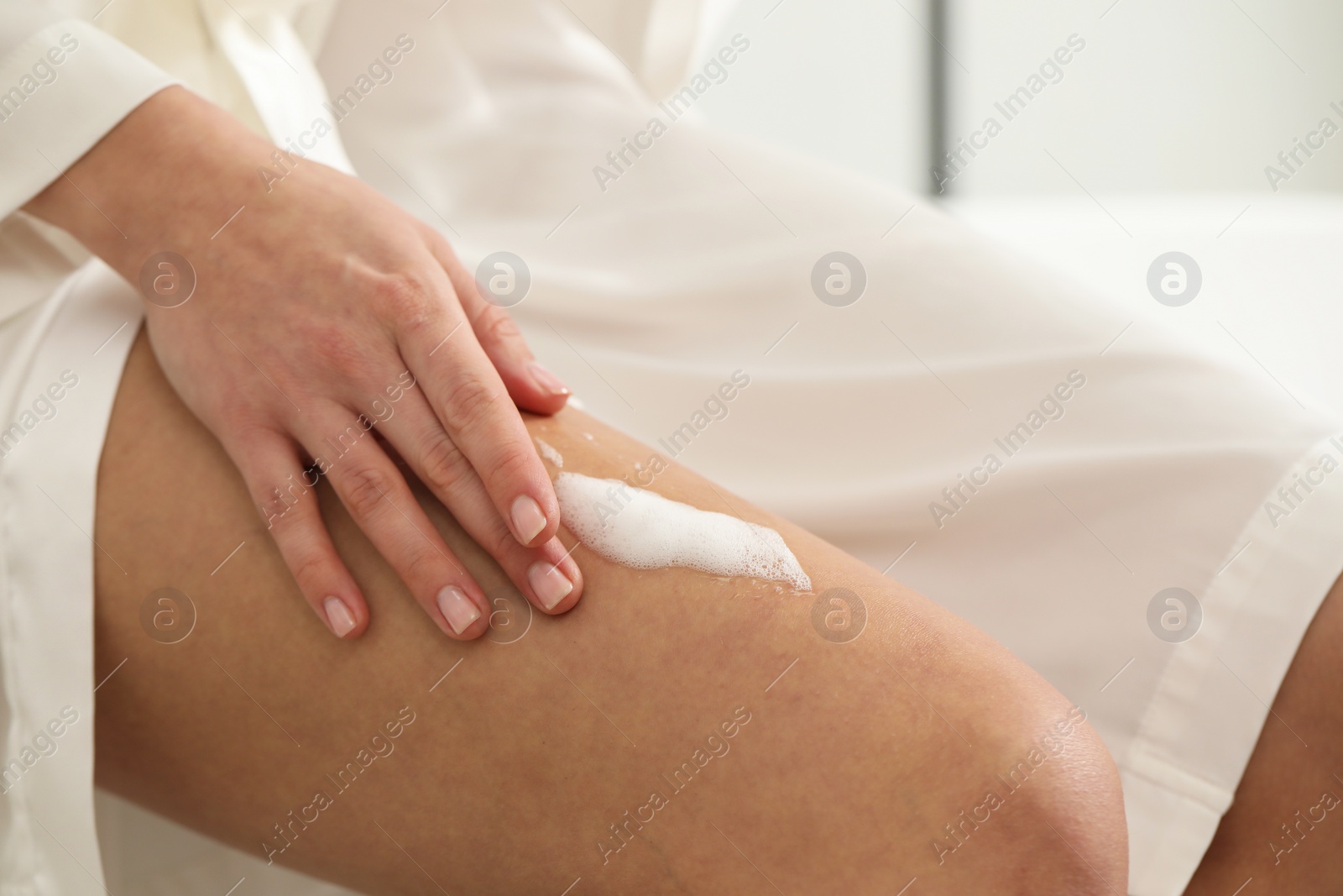 Photo of Woman applying self-tanning product onto leg indoors, closeup