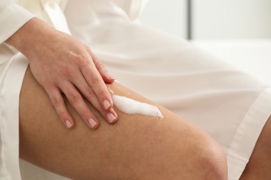 Photo of Woman applying self-tanning product onto leg indoors, closeup