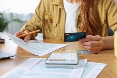 Photo of Woman with credit card calculating taxes at wooden table indoors, closeup