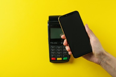 Photo of Woman with smartphone using modern payment terminal on yellow background, top view