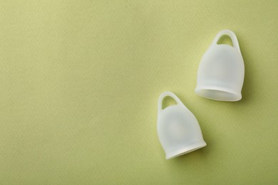 Photo of Menstrual cups on light green background, flat lay. Space for text