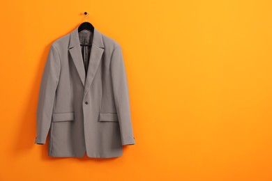 Hanger with grey jacket on orange wall, space for text