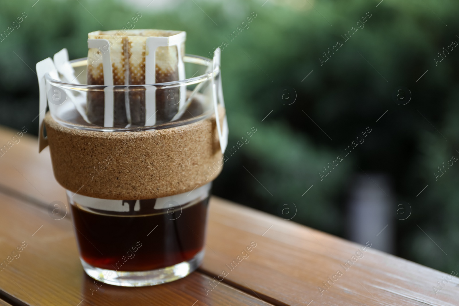 Photo of Glass cup with drip coffee bag on wooden table, closeup. Space for text