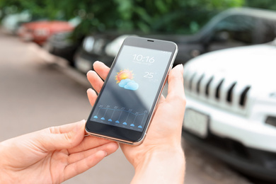 Woman using weather forecast app on smartphone outdoors, closeup