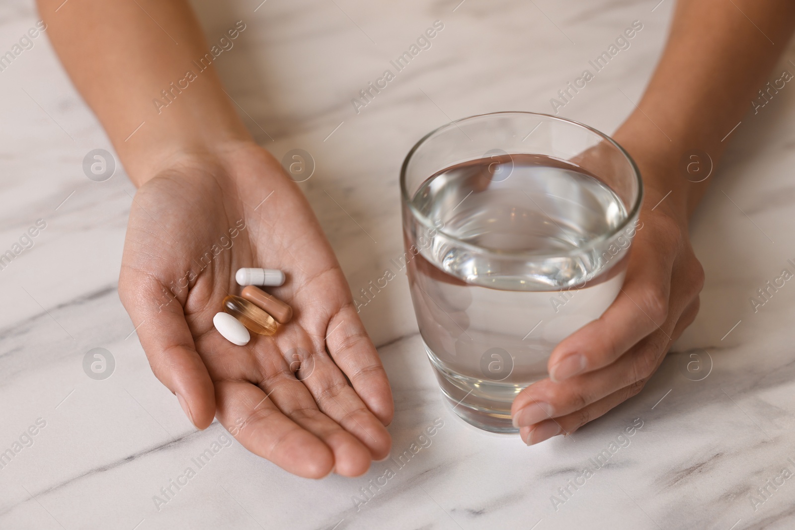 Photo of Woman with vitamin pills and glass of water at white marble table, closeup