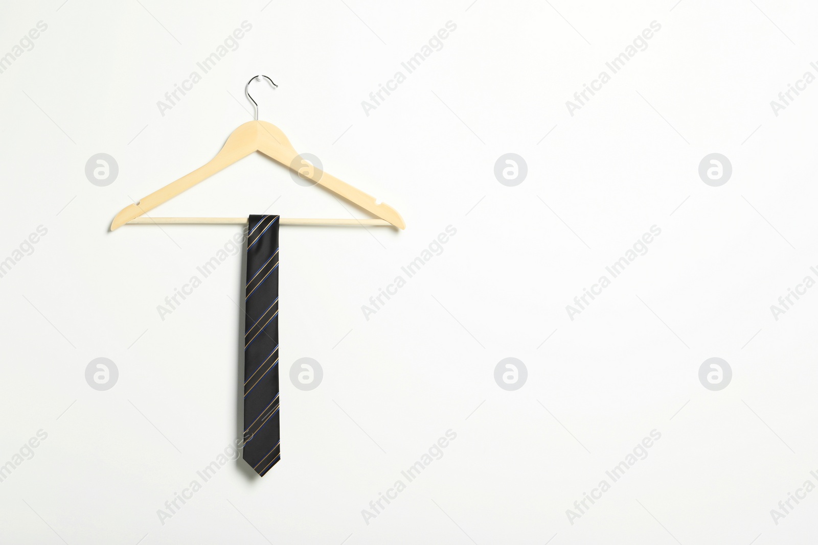 Photo of Hanger with striped necktie on white wall. Space for text