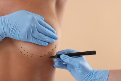 Breast augmentation. Doctor with marker preparing woman for plastic surgery operation against beige background, closeup. Space for text.