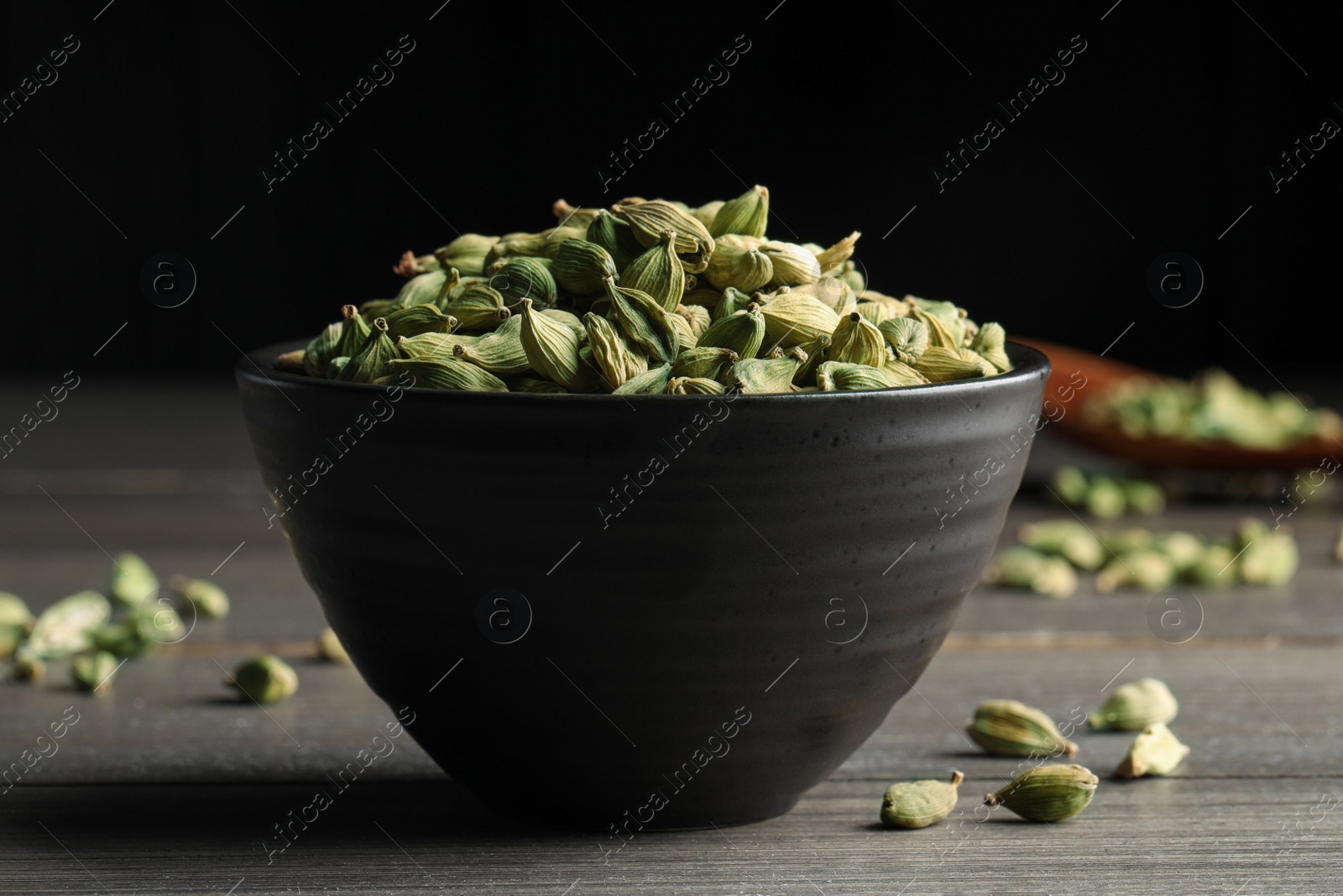 Photo of Bowl of dry cardamom pods on wooden table