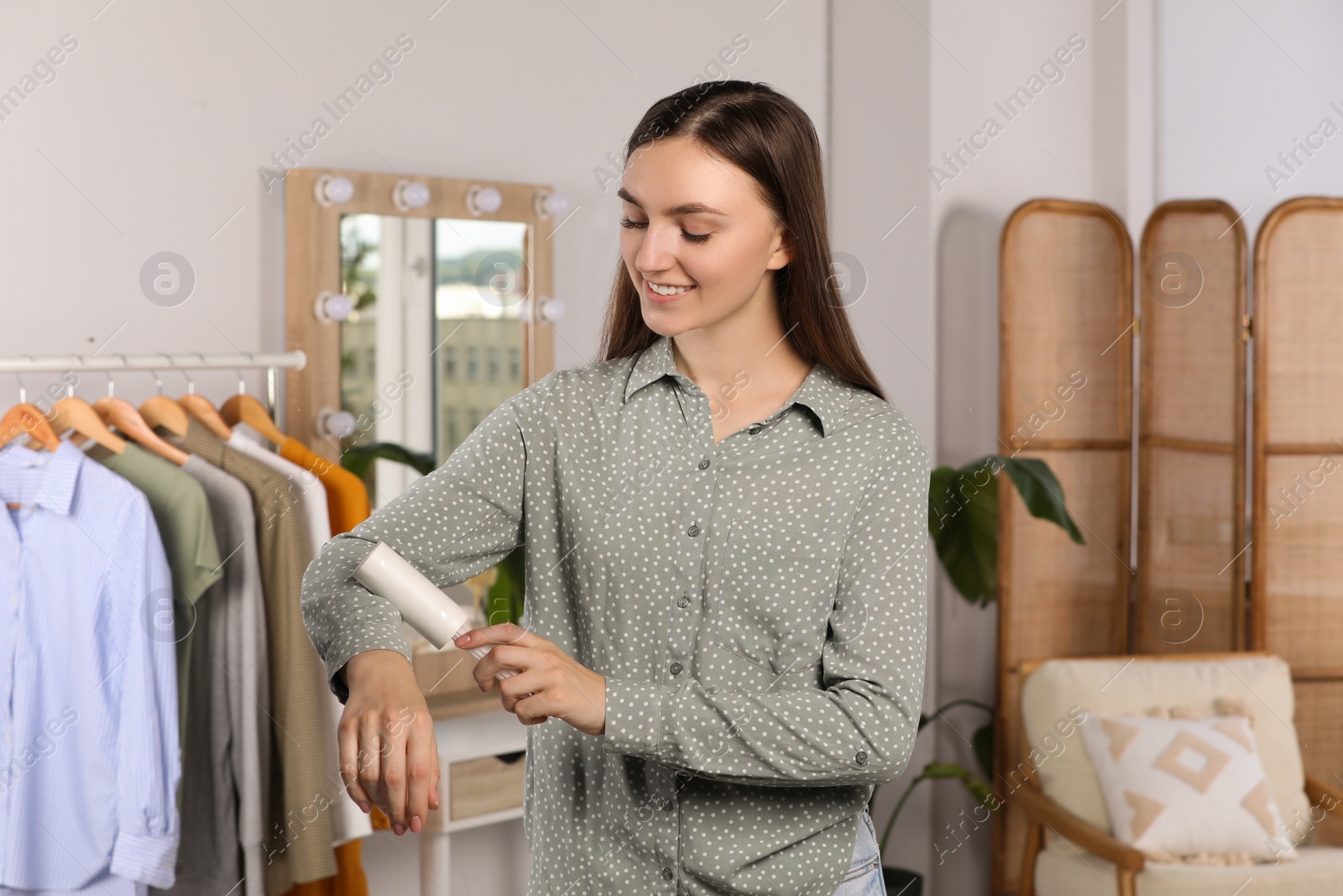 Photo of Young woman cleaning clothes with adhesive lint roller indoors