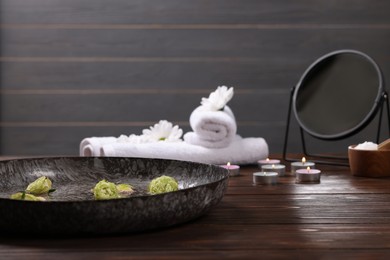 Photo of Bowl of water, flowers and burning candles on wooden table, space for text. Pedicure procedure