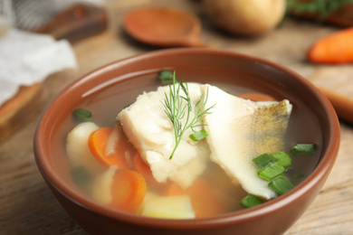 Photo of Delicious fish soup in bowl on wooden table, closeup