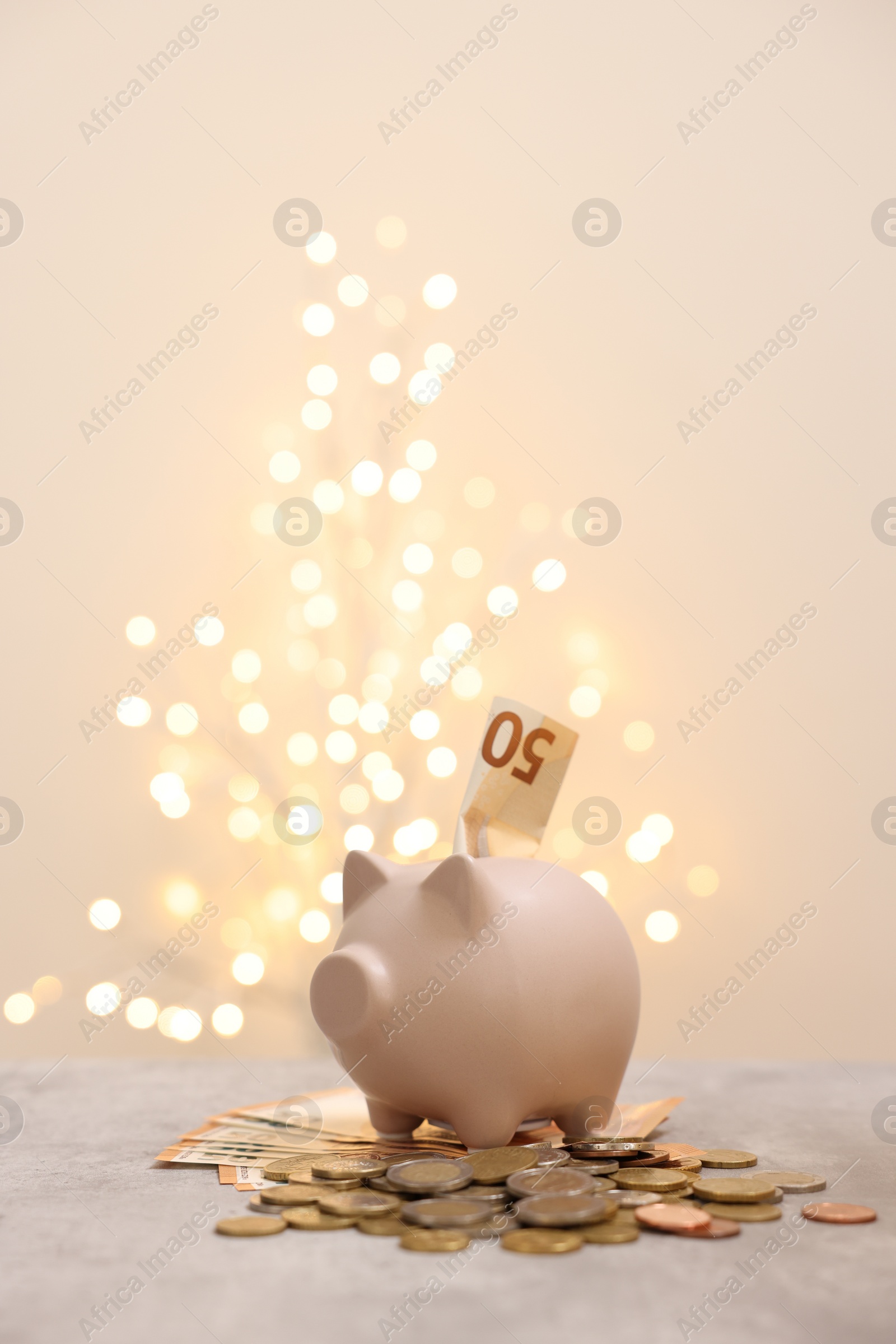 Photo of Piggy bank with euro banknote and coins on grey table against blurred lights, space for text