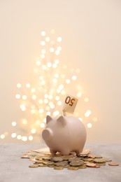 Piggy bank with euro banknote and coins on grey table against blurred lights, space for text