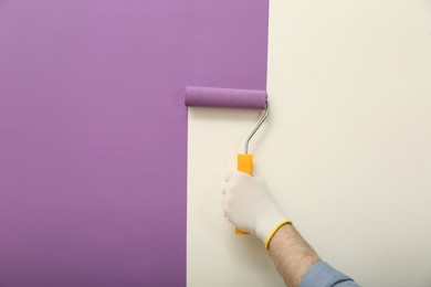 Man applying violet paint with roller brush on white wall, closeup