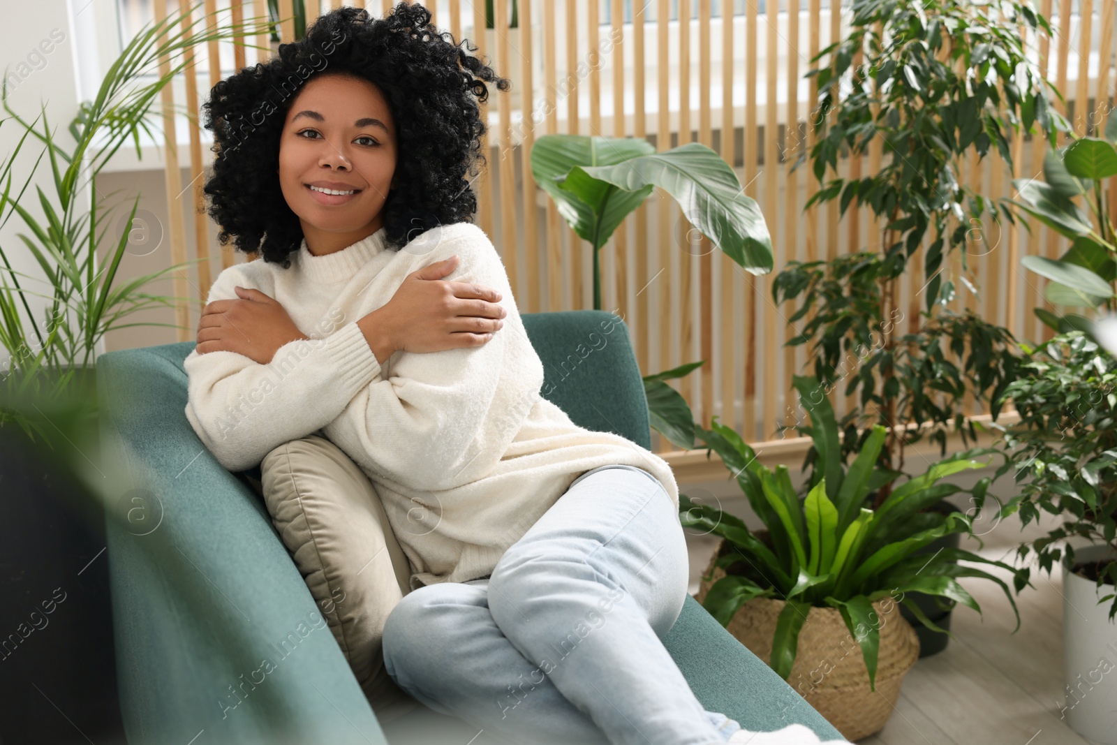 Photo of Happy woman relaxing on sofa near beautiful houseplants at home