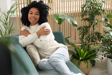 Photo of Happy woman relaxing on sofa near beautiful houseplants at home