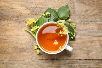 Photo of Cup of tea and linden blossom on wooden table, flat lay