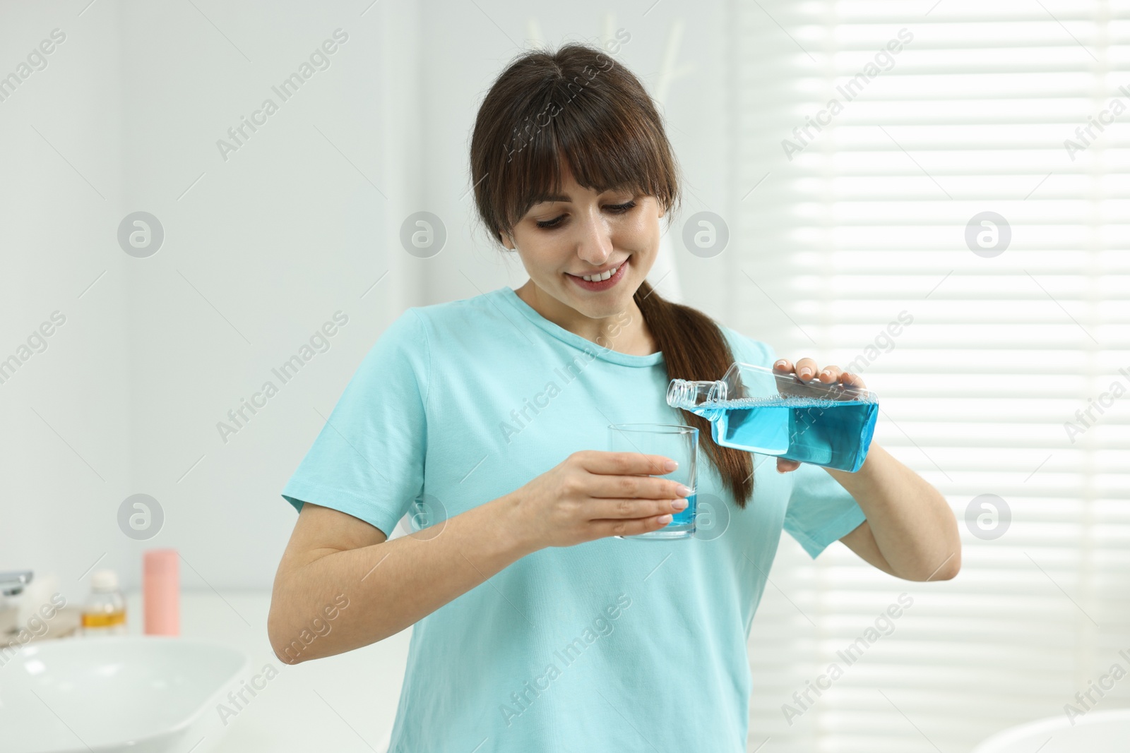 Photo of Young woman using mouthwash in bathroom. Oral hygiene