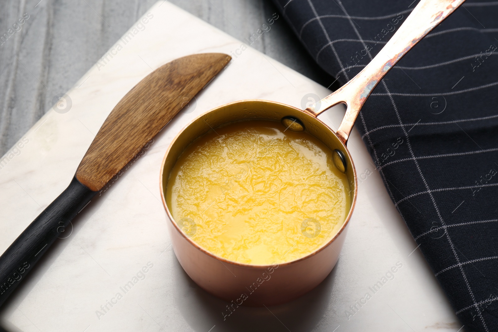 Photo of Stone board with saucepan of clarified butter and knife on table