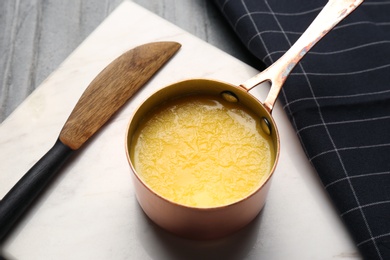 Photo of Stone board with saucepan of clarified butter and knife on table