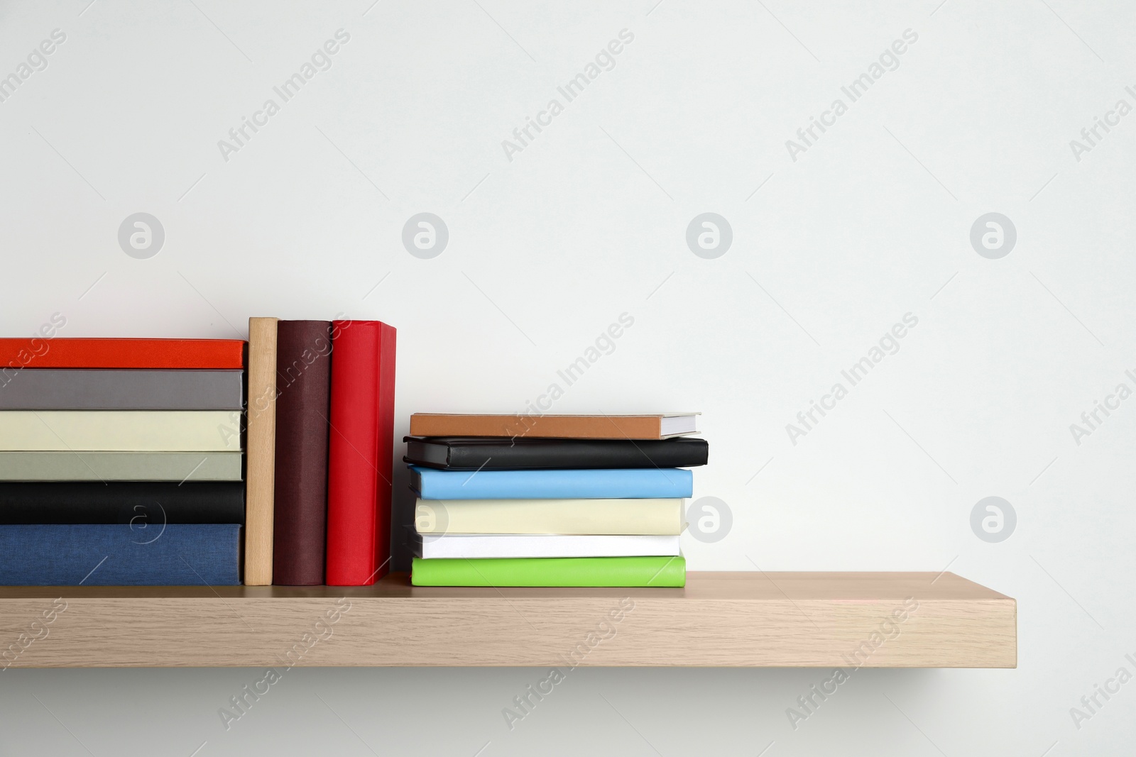 Photo of Many hardcover books on wooden shelf near white wall. Space for text