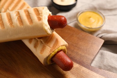 Photo of Tasty french hot dogs and dip sauce on wooden board, closeup. Space for text
