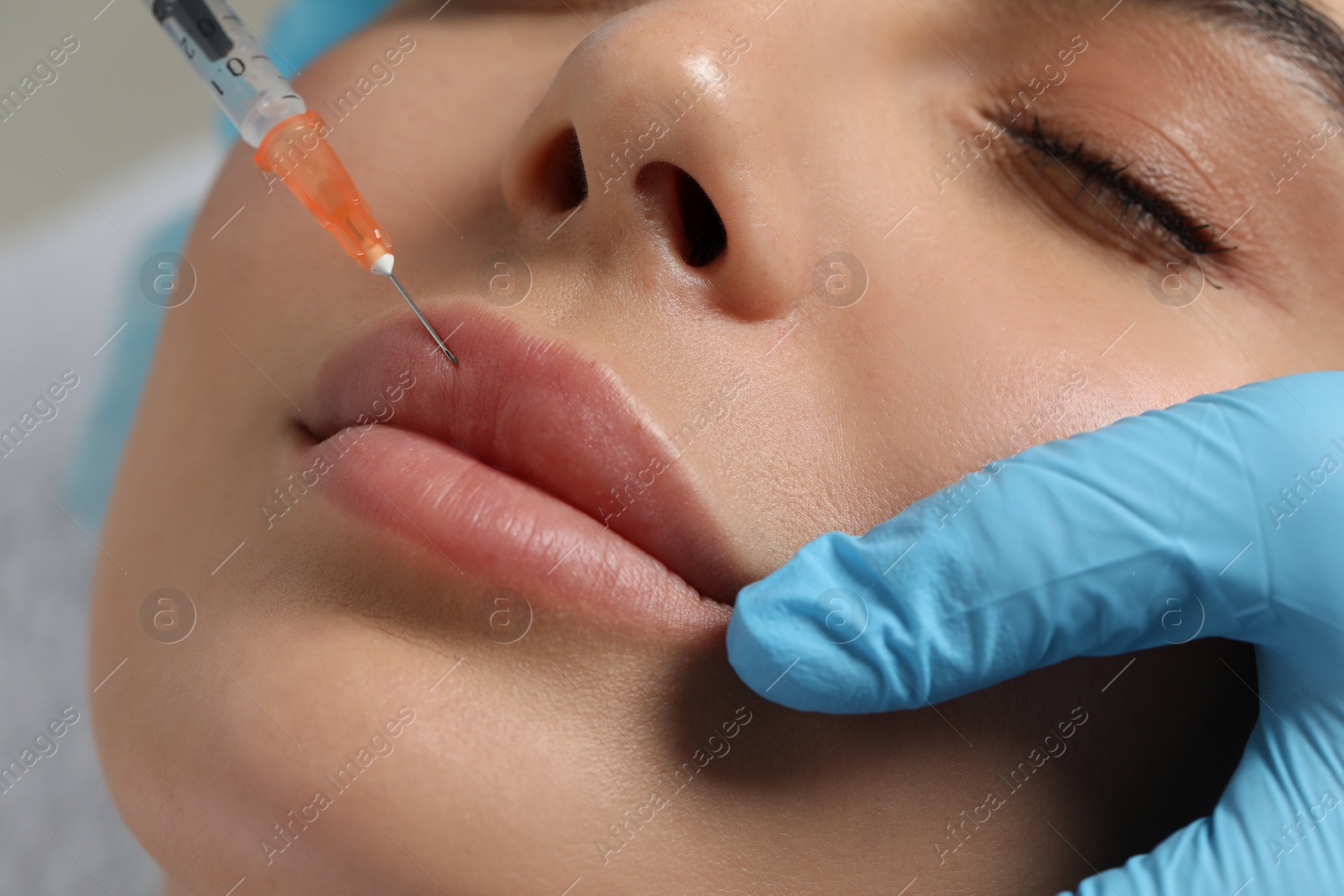 Photo of Doctor giving lips injection to young woman in clinic, closeup. Cosmetic surgery