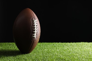 Photo of Leather American football ball on green grass against black background. Space for text