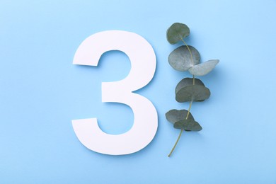 Paper number 3 and eucalyptus branch on light blue background, top view