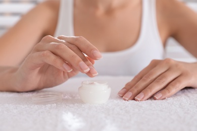 Photo of Woman taking cream from jar on white towel, closeup