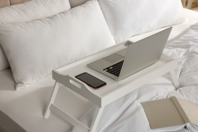 Photo of White tray with modern laptop and smartphone on bed indoors