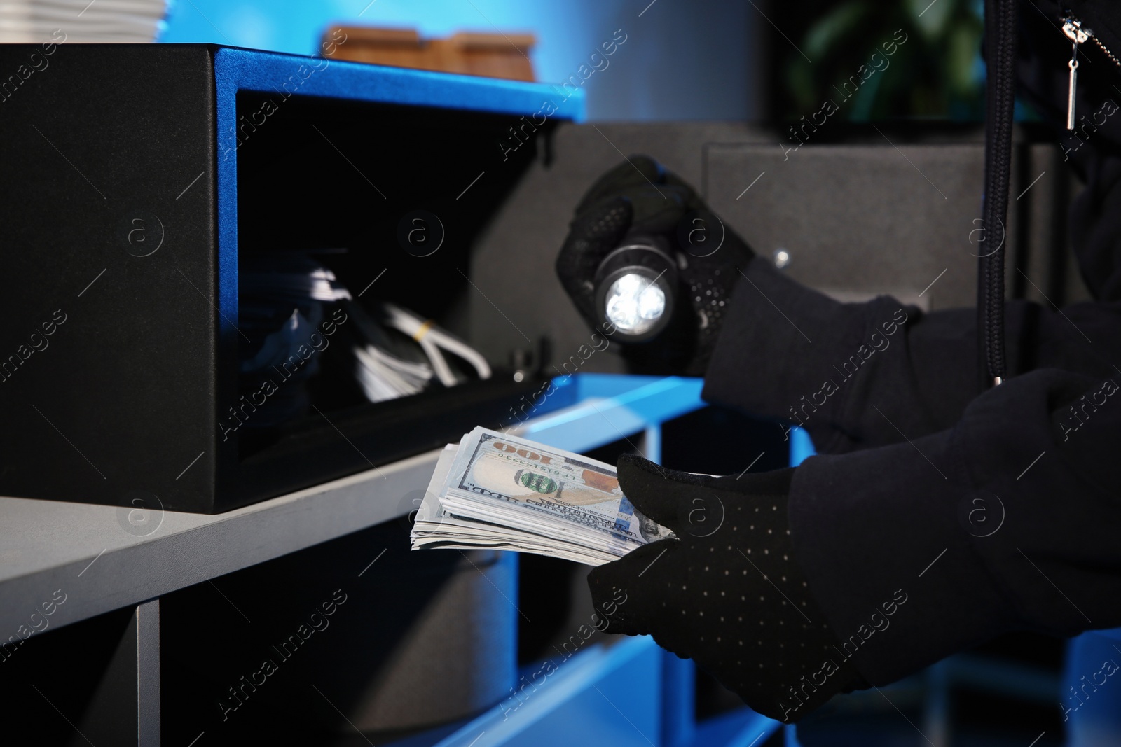 Photo of Thief taking money out of steel safe indoors at night, closeup