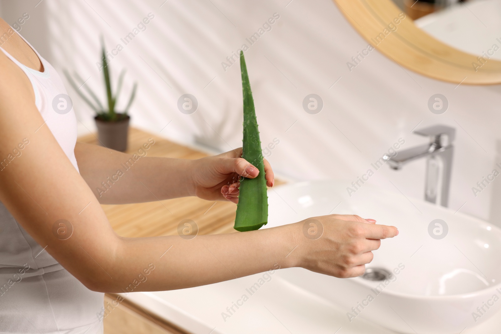 Photo of Young woman applying aloe gel from leaf onto her arm in bathroom, closeup