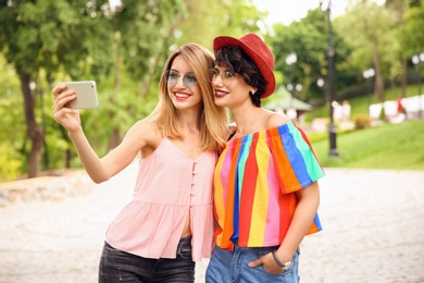 Photo of Young women in stylish clothes taking selfie outdoors
