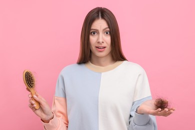 Photo of Emotional woman holding brush with lost hair on pink background. Alopecia problem