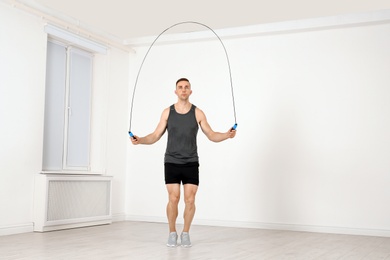 Full length portrait of young sportive man training with jump rope in light room