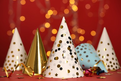 Party hats and festive items on table against red background with blurred lights