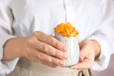 Photo of Young woman holding jar of tasty chia seed pudding with persimmon, closeup