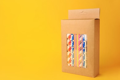 Photo of Box with many paper drinking straws on orange background. Space for text