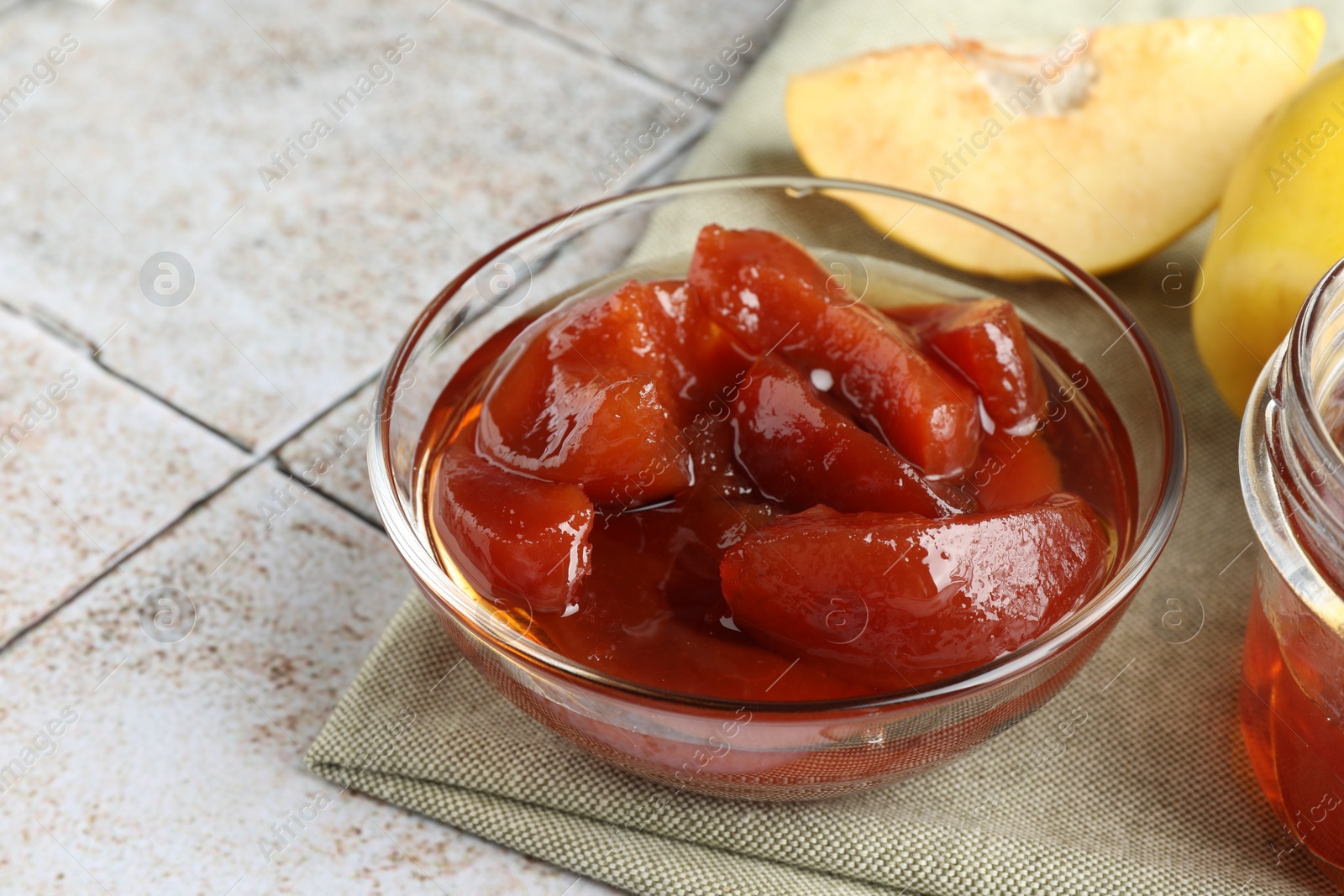 Photo of Tasty homemade quince jam in bowl and fruits on tiled table, closeup. Space for text