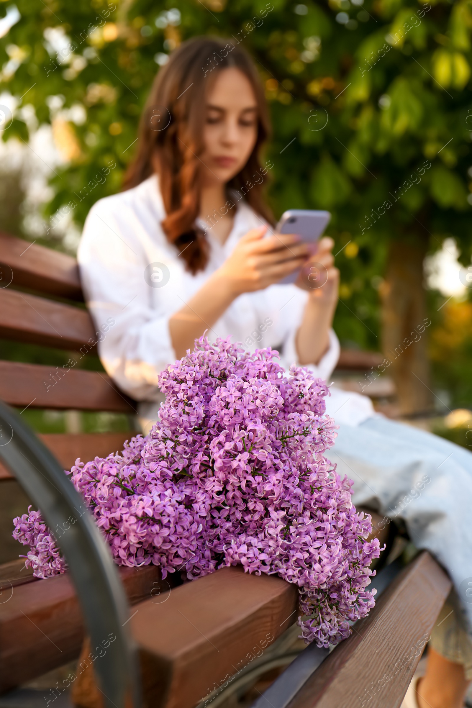 Photo of Attractive young woman with mobile phone in park, focus on lilac flowers