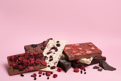 Different chocolate bars with freeze dried fruits on pink background, space for text