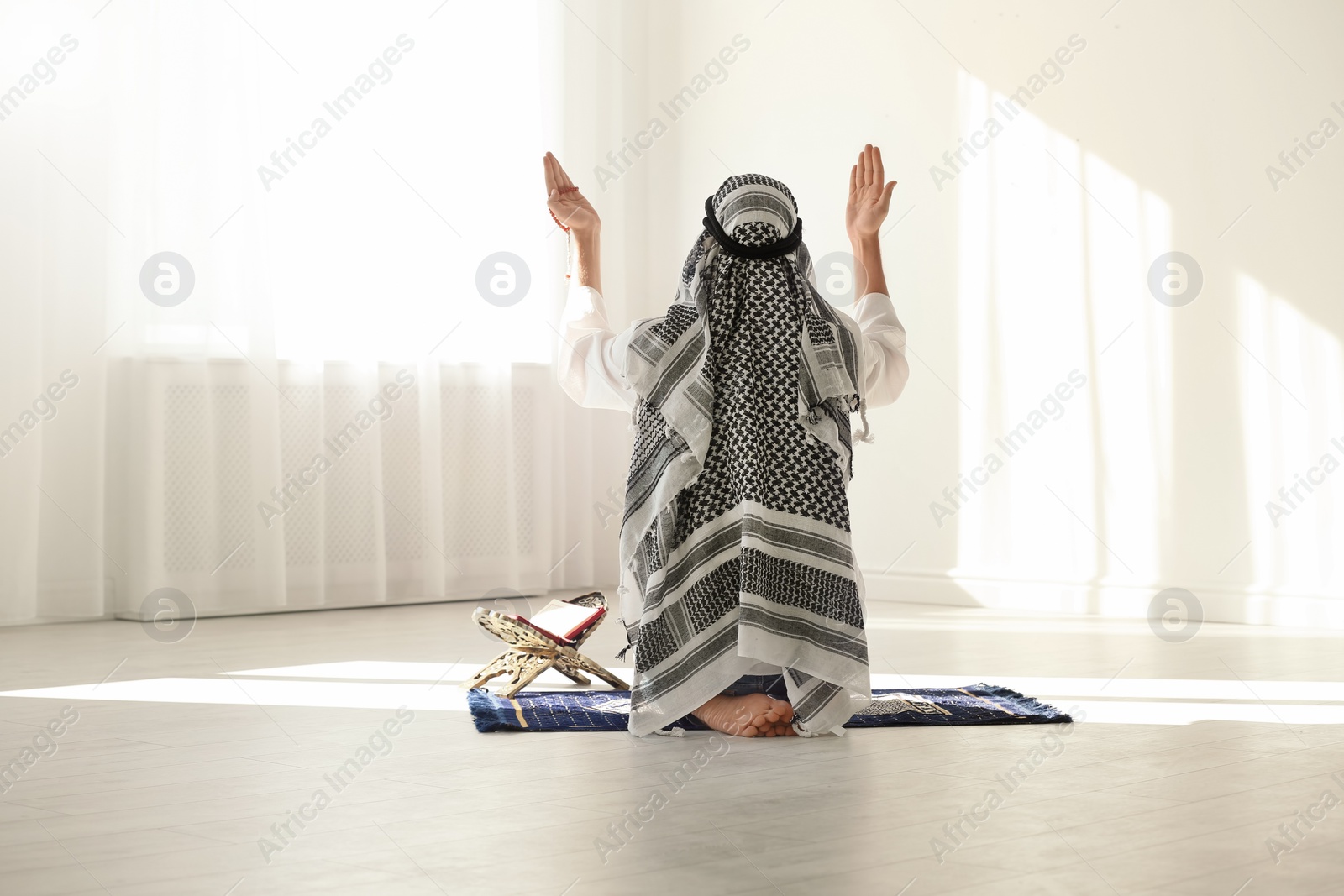 Photo of Muslim man in traditional clothes praying on rug indoors