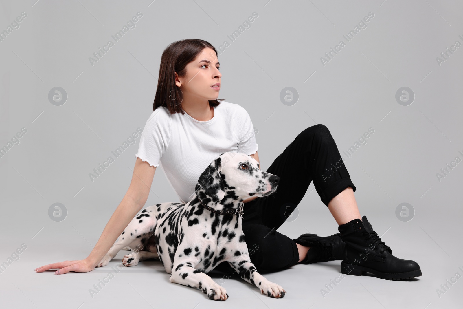 Photo of Beautiful young woman with her adorable Dalmatian dog on light grey background. Lovely pet