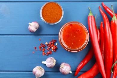 Photo of Spicy chili sauce in jar and ingredients on blue wooden table, flat lay. Space for text