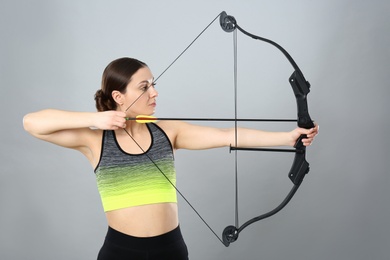 Photo of Sporty young woman practicing archery on light grey background