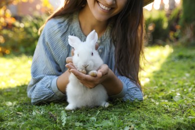 Photo of Happy woman with cute rabbit on green grass outdoors, closeup