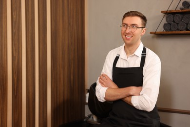 Photo of Professional hairdresser wearing apron in beauty salon, space for text